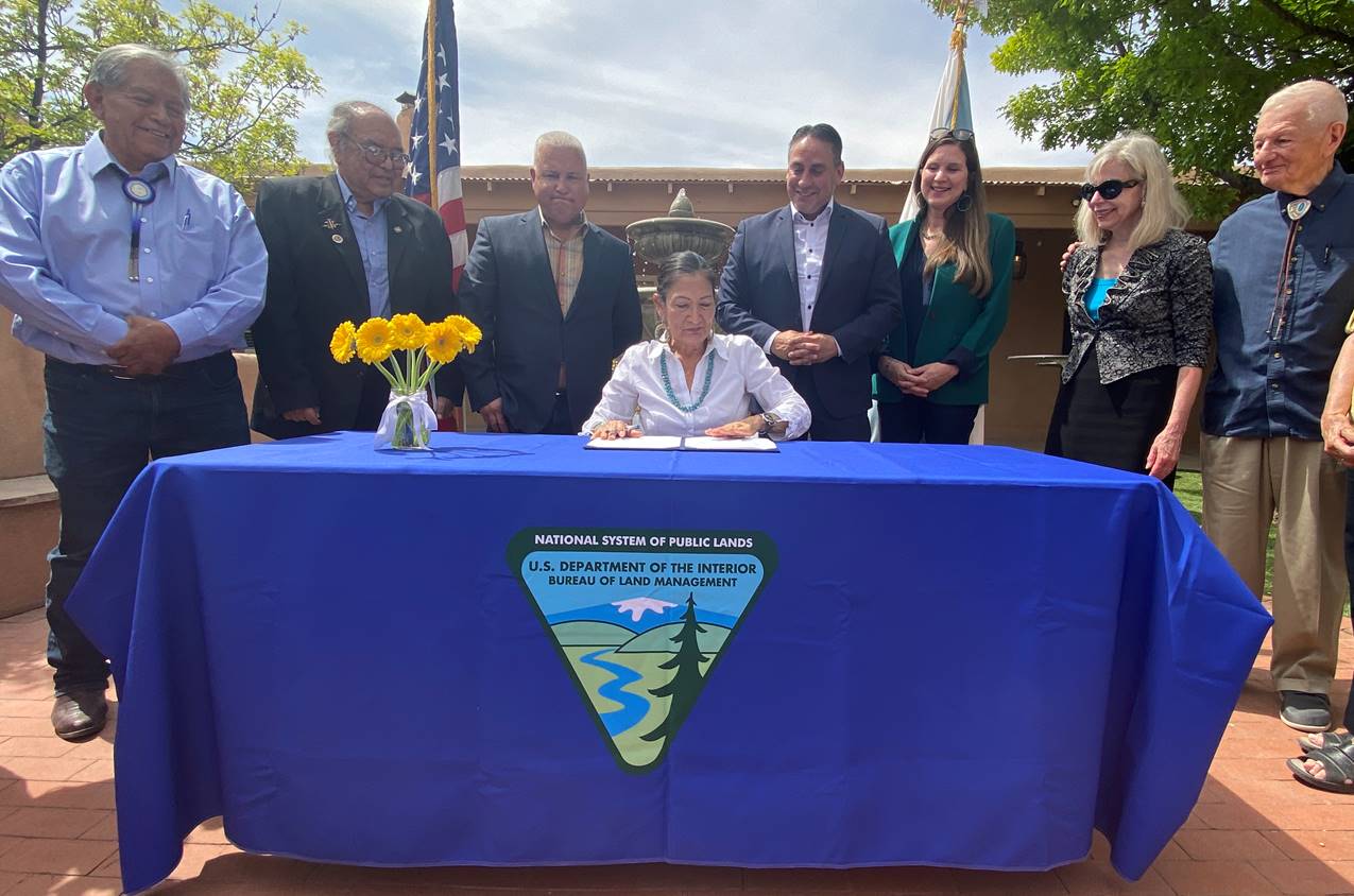 Secretary Haaland signing document at a table with others standing behind her. 